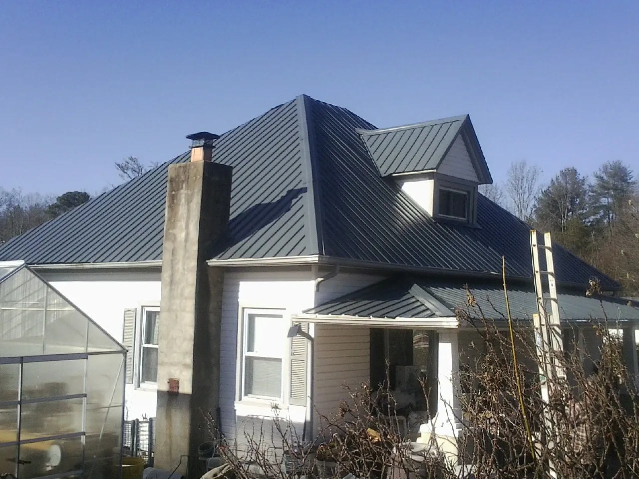 Dark blue standing seam metal roof on a white farmhouse with dormer — Slate & Tile Roof Repair by Roofing Brothers in Hudsonville