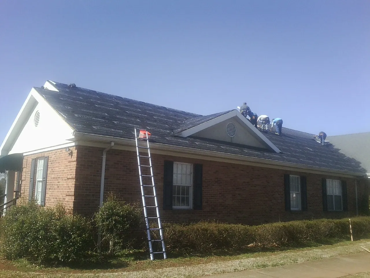 Crew tearing shingles off a brick ranch roof with a ladder set — Emergency Roof Repair work by our crew in Hudsonville