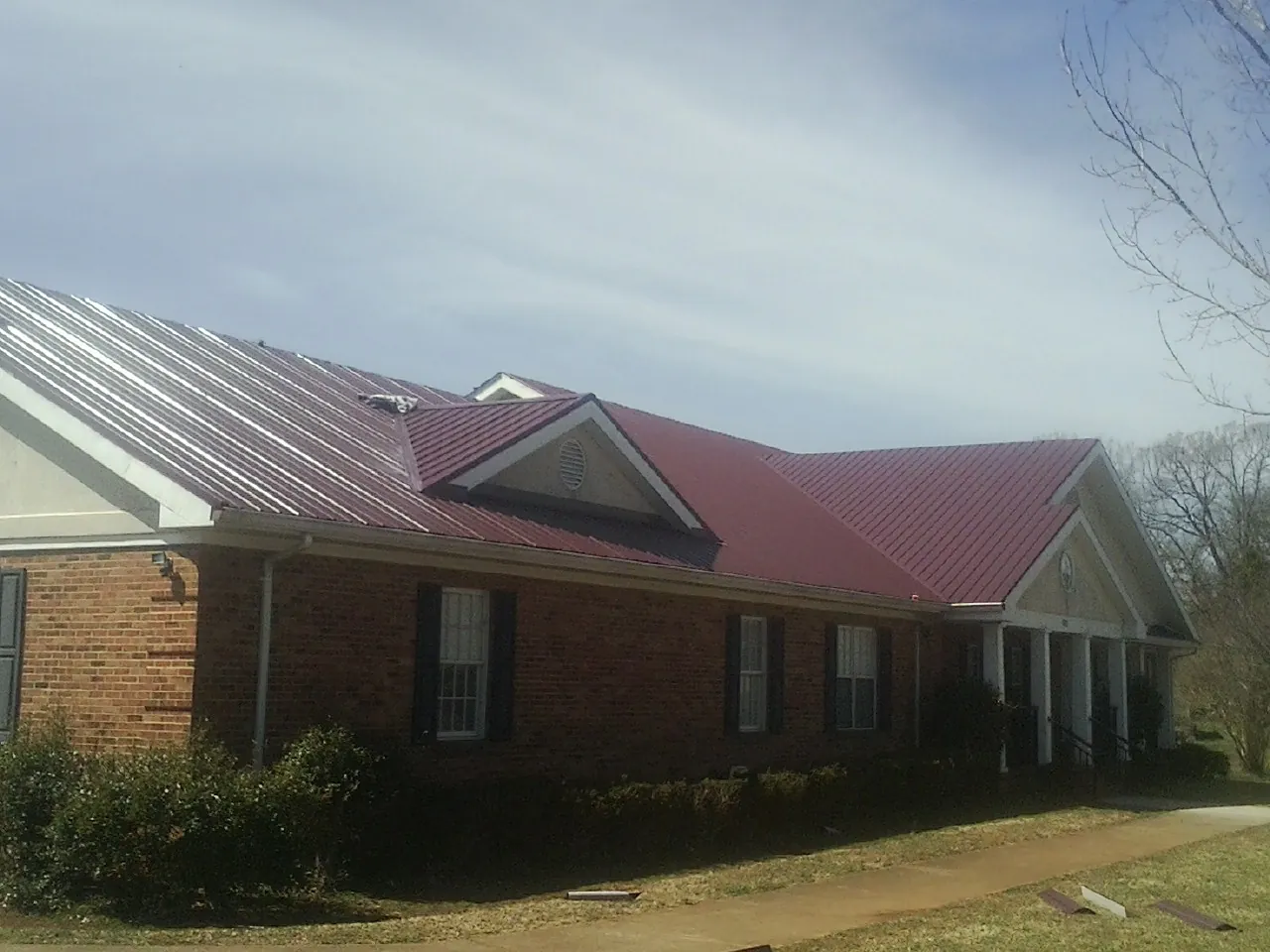 Red metal roof with gabled entries on a long brick building, from a Hail Damage Roof Repair job in Hudsonville