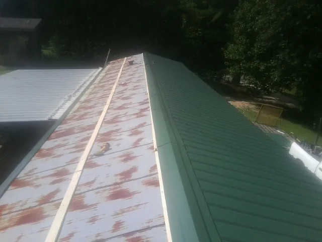 Old rusted panels beside newly installed green metal roofing — Wind Damage Roof Repair by Roofing Brothers in Hudsonville