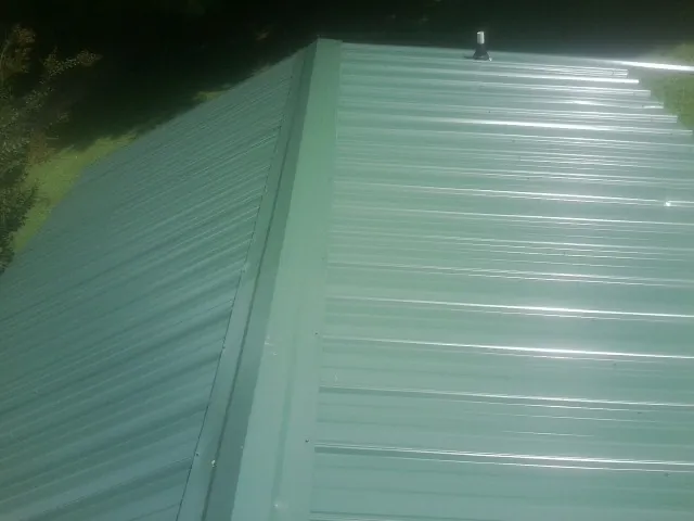 New green metal panels meeting at the ridge of a roof — Flat Roof Repair work by our crew in Hudsonville