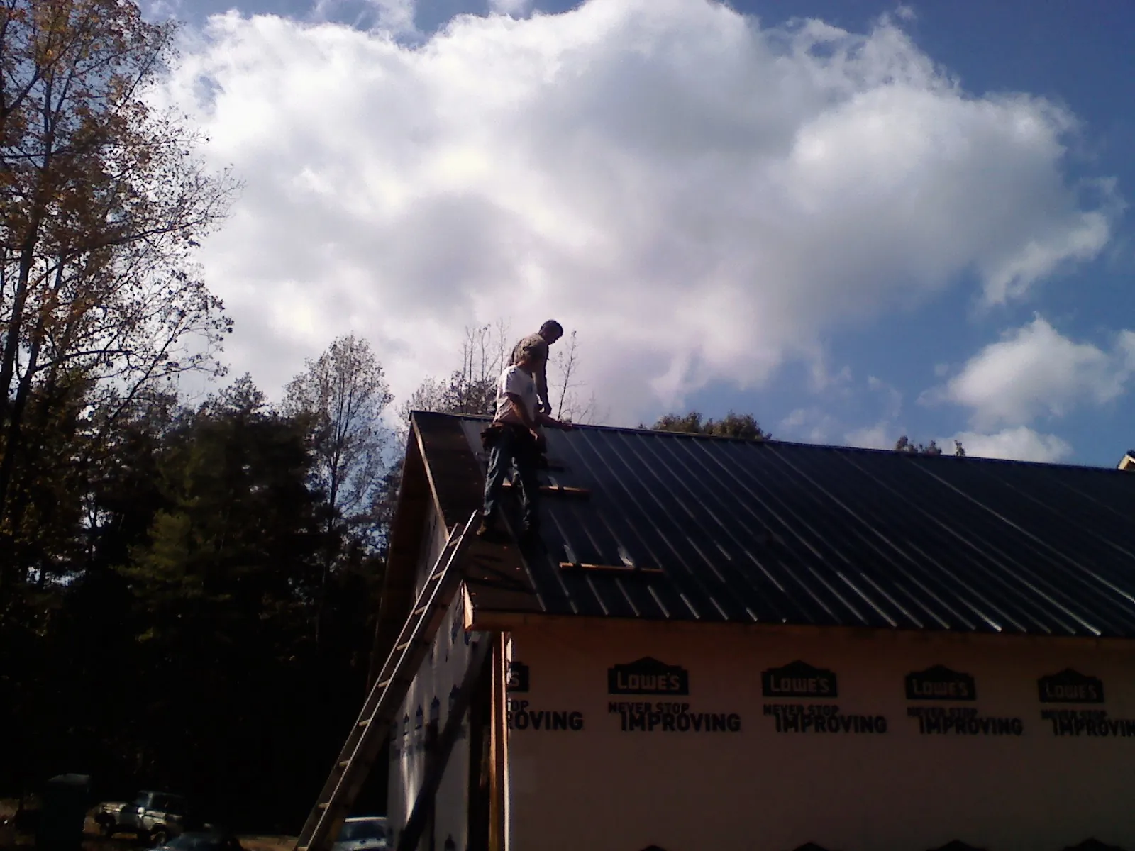 Roofer fastening dark metal panels high against a cloudy sky, from a Roof Inspection job in Hudsonville