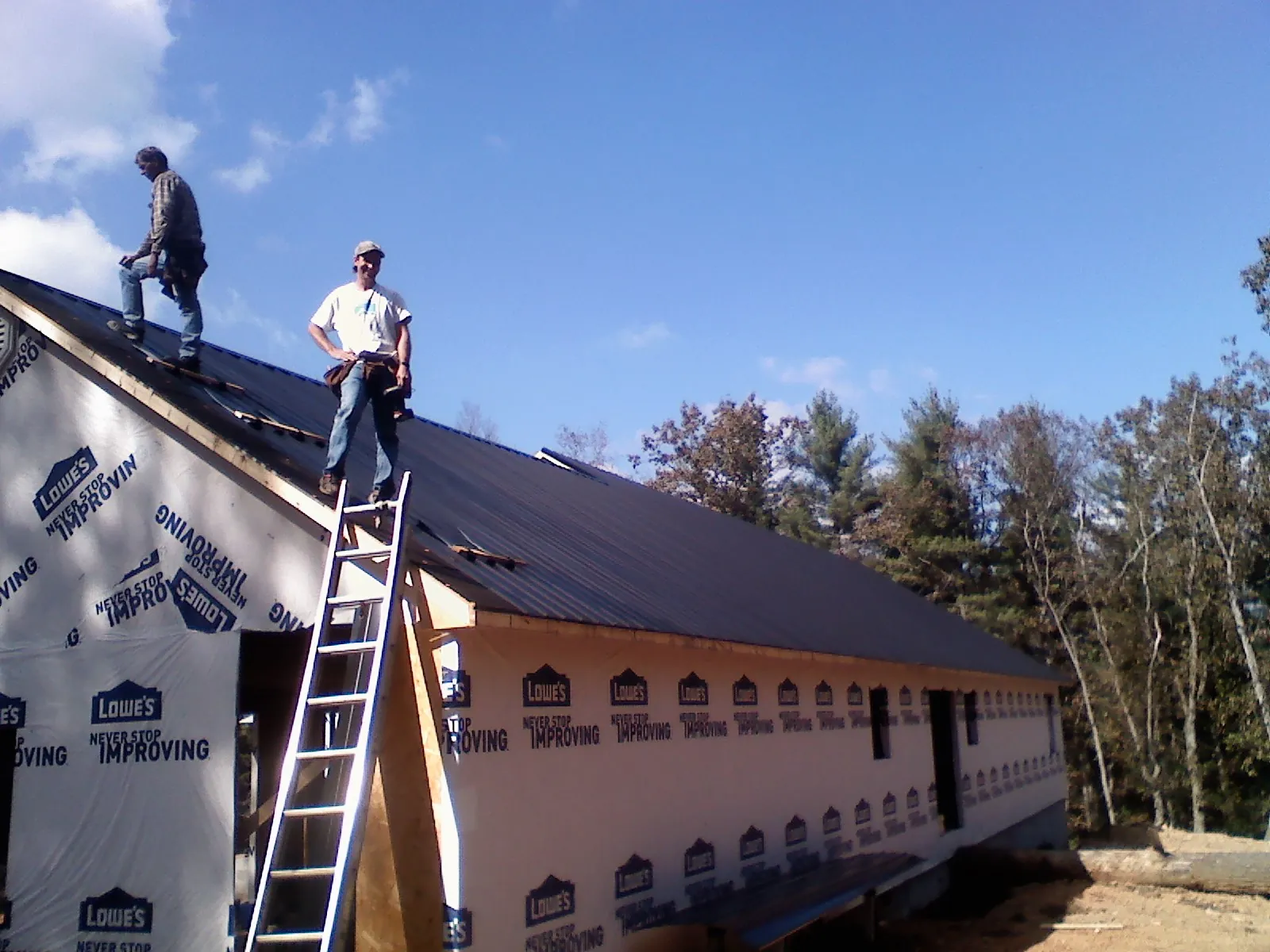 Two roofers standing on a long dark metal roof over a wrapped building in Hudsonville