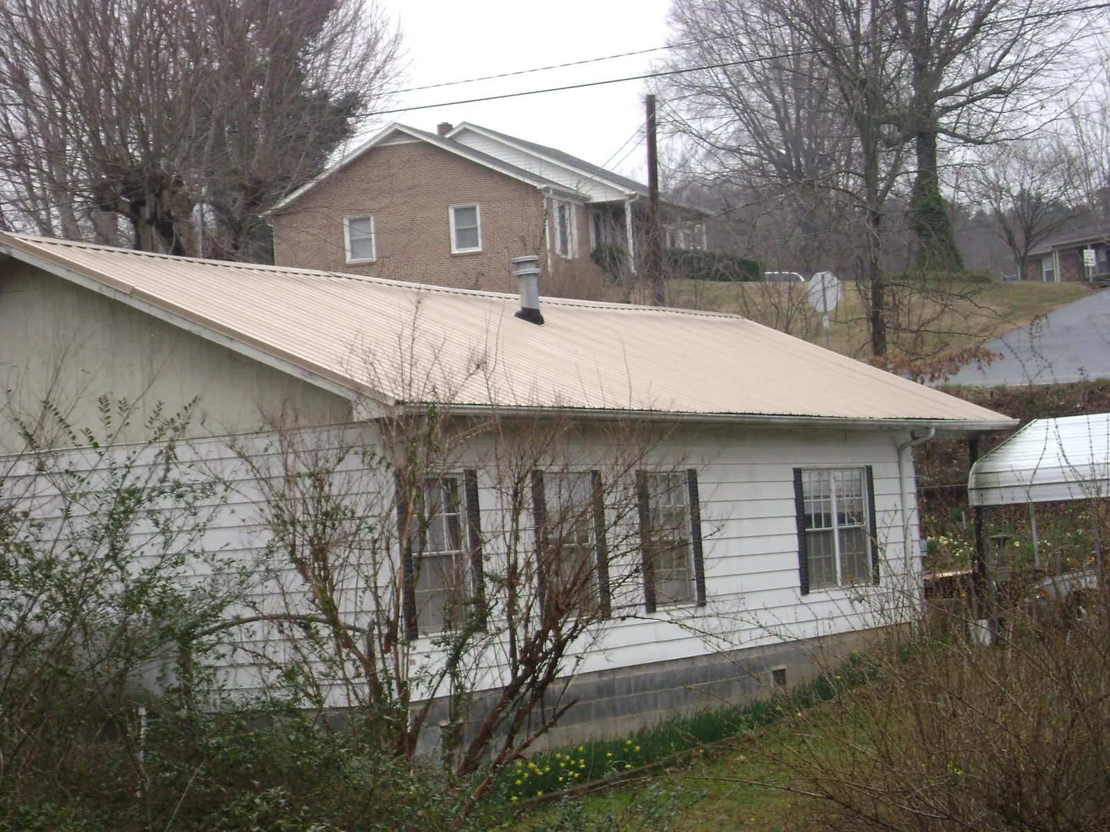 Tan metal roof on a white sided house set into a hillside — Commercial Roofing by Roofing Brothers in Hudsonville